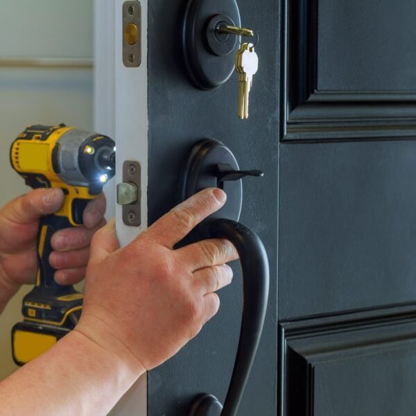 Closeup of a professional locksmith installing a new lock on a house exterior door with the inside e1633675647428